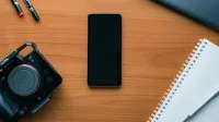Una ordenada y plana de un espacio de trabajo moderno con un teléfono inteligente, cámara, bolígrafos y portátil.