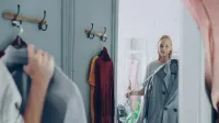 Mujer sosteniendo una chaqueta, reflexionando en el espejo de una tienda, decidiendo sobre su atuendo.