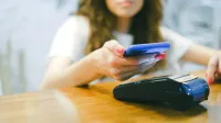Una mujer procesa un pago sin contacto usando su teléfono inteligente en una terminal de pago.