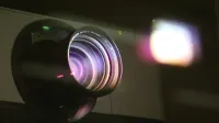 Vista detallada de una lente de proyector que emite luz, mostrando tecnología óptica.