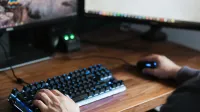 High angle crop male in casual clothes sitting at desk and browsing contemporary computer while typing on backlit keyboard and using mouse