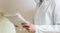 Doctor in a white coat examining medical papers in a healthcare setting.