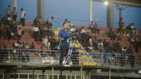Camarógrafo en la plataforma capturando imágenes en un evento de estadio lleno de gente.