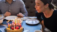 Una mujer soplando con alegría las velas en un pastel de cumpleaños con tapa de frutas, compartiendo un momento festivo.