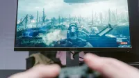 Una persona que juega un videojuego en un monitor de alta resolución, mostrando un paisaje de guerra.