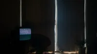 Una sala de estar con poca luz con estática en la televisión y cortinas hechas, creando una atmósfera de mal humor.