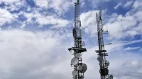 Torres de telecomunicaciones con antenas y platos bajo un cielo nublado brillante.