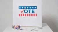 urna con signo de voto rodeado de pegatinas de votación, indicando tema electoral.