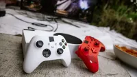 Controladores de juegos inalámbricos blancos y rojos en una superficie texturizada cerca de chips y una pantalla de TV.