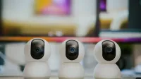 Three modern smart home security cameras placed on a table indoors with a blurry background.