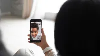 Vista posterior de una pareja anónima comunicándose con un niño afroamericano a través de video chat en un teléfono inteligente moderno mientras se sienta en la sala de estar en un fondo