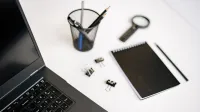 Un moderno espacio de trabajo de oficina con una computadora portátil, un cuaderno y papelería en un escritorio blanco.