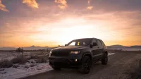 Un SUV robusto que conduce en un camino rural nevado bajo un hermoso cielo de puesta de sol.