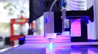 Close-up of a laser engraving machine working indoors with blue light reflection.