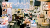 Cálido interior de una pequeña y acogedora tienda en Osaka, con una mujer asiática que trabaja, rodeada de productos locales y decoración.