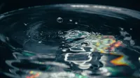 Close-up of a water droplet causing ripples with colorful prism reflection, captured in detail.