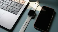 Flat lay of a laptop, smartwatch, and smartphone on a blue surface, highlighting modern technology.