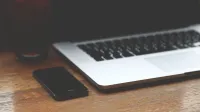 Un espacio de trabajo minimalista con una computadora portátil y un teléfono inteligente en un escritorio de madera.
