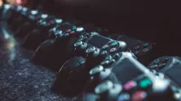 Serie de controladores de juegos alineados en una superficie reflectante, con poca luz.
