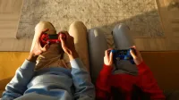 Dos personas que usan controladores de juego mientras están sentados en un sofá amarillo, enfocados en los juegos.