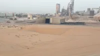 Paisaje desértico con almacén industrial y estructuras de fábrica.