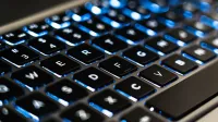 Detailed view of a backlit laptop keyboard keys with blue LED lighting for tech concepts.