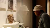 Adult male observes ancient artifact display in a museum, reflecting history and learning.