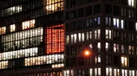 Vista nocturna de un edificio urbano con ventanas iluminadas y un distintivo cartel rojo. Perfecto para el paisaje urbano y temas arquitectónicos.