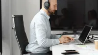 Un agente de centro de llamadas enfocado con auriculares trabajando en una computadora portátil en una oficina.