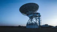Un gran radiotelescopio bajo un cielo despejado capta señales cósmicas.