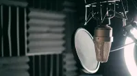 Primer plano de un micrófono de condensador con filtro pop en un estudio de sonido profesional.