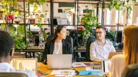 Un equipo diverso de profesionales discutiendo proyectos en un entorno de oficina lleno de plantas.