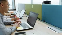 Colleagues working diligently at shared desks with laptops in a modern office space.