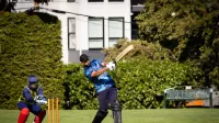 Cricketer hitting the ball with wicketkeeper ready during an outdoor cricket match.