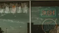 Signo de sushi de neón y reflexión en la ventana del restaurante con cielo nublado.