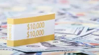 Primer plano de una pila de billetes de $10,000 dólares estadounidenses con una correa de moneda en un fondo de papel moneda.