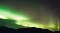 Vista de paisaje de ángulo bajo de las luces del norte verde brillante iluminando la silueta de la montaña y el cielo estrellado en la noche