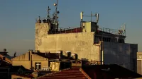 A city rooftop with antennas and relay towers against a clear blue sky at sunset.