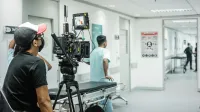 Cameraman capturing a scene in a hospital corridor with a professional video camera.