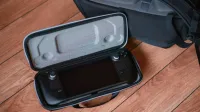 Una consola de juegos portátil en una funda protectora sobre suelo de madera con mochila.