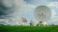 Una variedad de grandes antenas parabólicas en un exuberante campo verde bajo un cielo nublado.