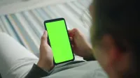 Close-up of person using phone with green screen for custom content display.