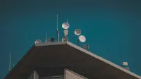Una vista de ángulo bajo de platos de comunicación y antenas en un edificio contra un cielo azul claro.