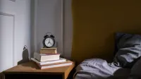 Un acogedor entorno de dormitorio con libros y un despertador en una mesita de noche junto a una cama.