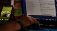 Close-up of a person working on a laptop and smartphone in a dimly lit office, showcasing remote work.