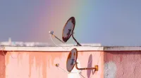 Two rusty satellite dishes on a rooftop against a vibrant rainbow in Tunisia.