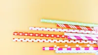 Pajitas de papel vibrantes con lunares y rayas sobre fondo amarillo.