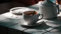 Taza de café blanco y olla sobre una mesa bañada por el sol, creando un ambiente acogedor.