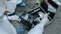 Experto forense que examina evidencia con herramientas en una investigación de la escena del crimen al aire libre.