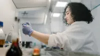 Mujer en bata de laboratorio realizando investigaciones con pipeta en laboratorio moderno.